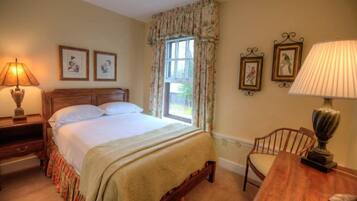 A bedroom with a bed, a nightstand, a chair, a table, and a window with curtains.