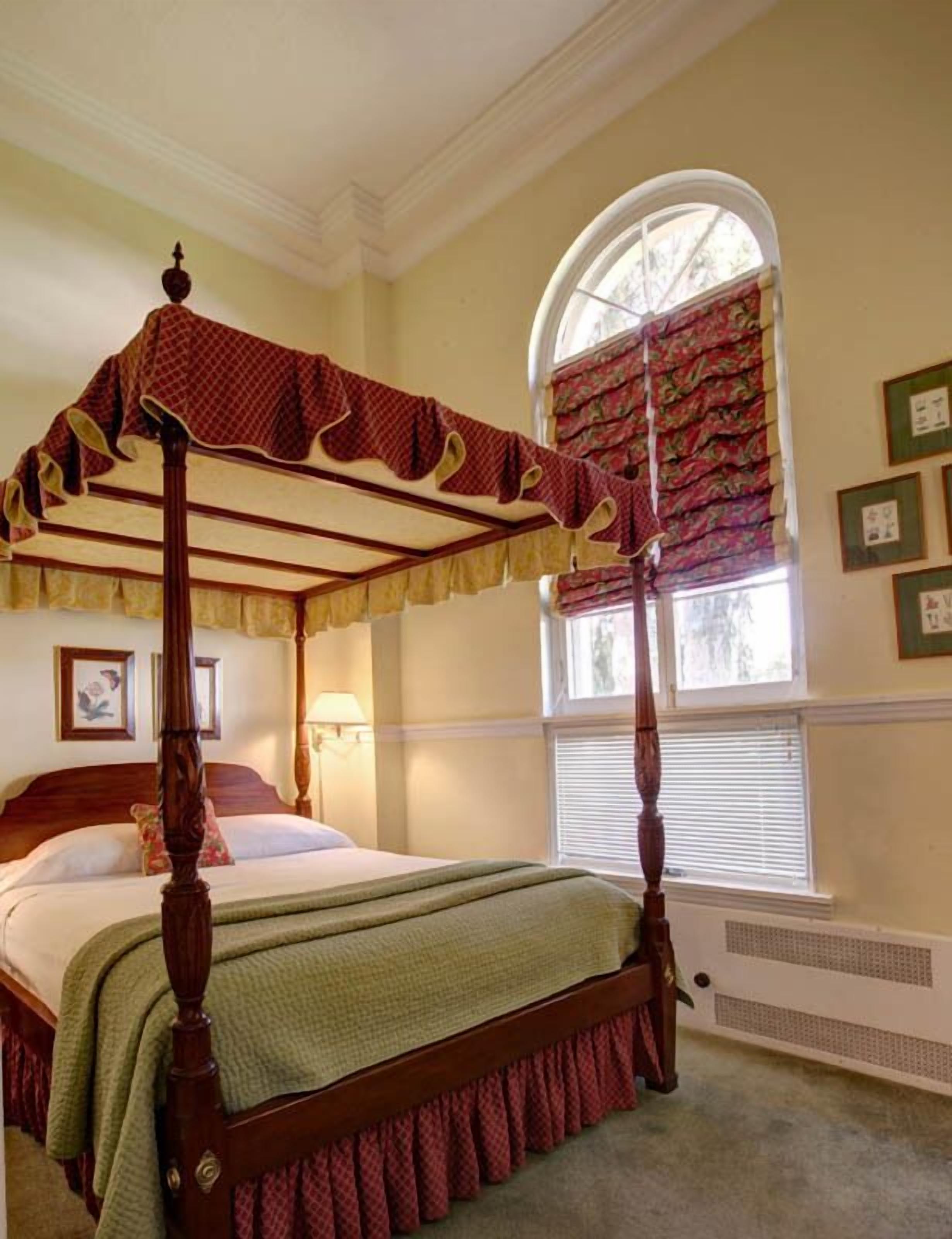 A four-poster bed with a canopy, a large window with curtains, and framed pictures on the wall.