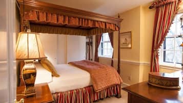 A traditional bedroom with a canopy bed, a bedside table with a lamp, and a window with curtains.