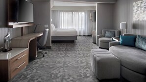 Une chambre d’hôtel moderne équipée d’une télévision à écran plat, d’un bureau avec des tiroirs, d’un canapé confortable, d’un lit et d’une grande fenêtre avec des rideaux.