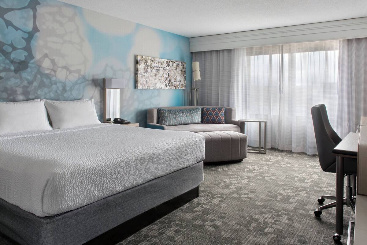 Ein Hotelzimmer mit einem großen Bett, einer Couch, einem Schreibtisch und einer Lampe.