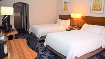 A hotel room with two beds, a desk with a lamp, a coffee maker, and a door leading to another room.