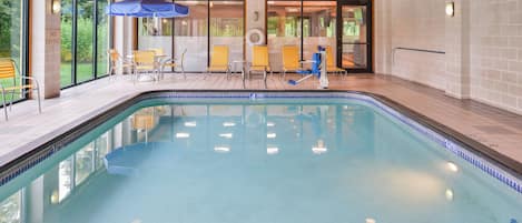 An indoor swimming pool with tiled walls, wooden ceiling beams, and several lounge chairs and umbrellas.