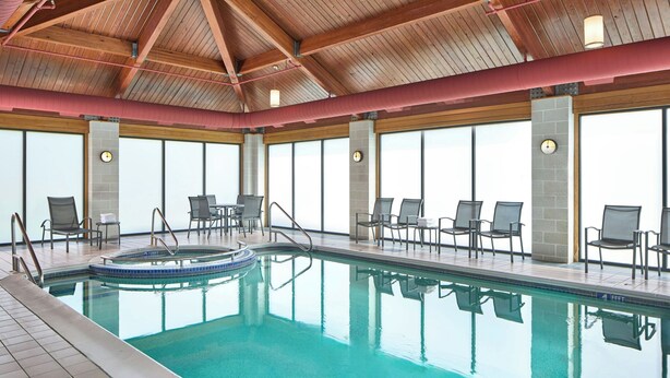 An indoor swimming pool with clear water, surrounded by lounge chairs and a high ceiling with wooden beams. - Fairfield Inn by Marriott Rochester East (Webster)