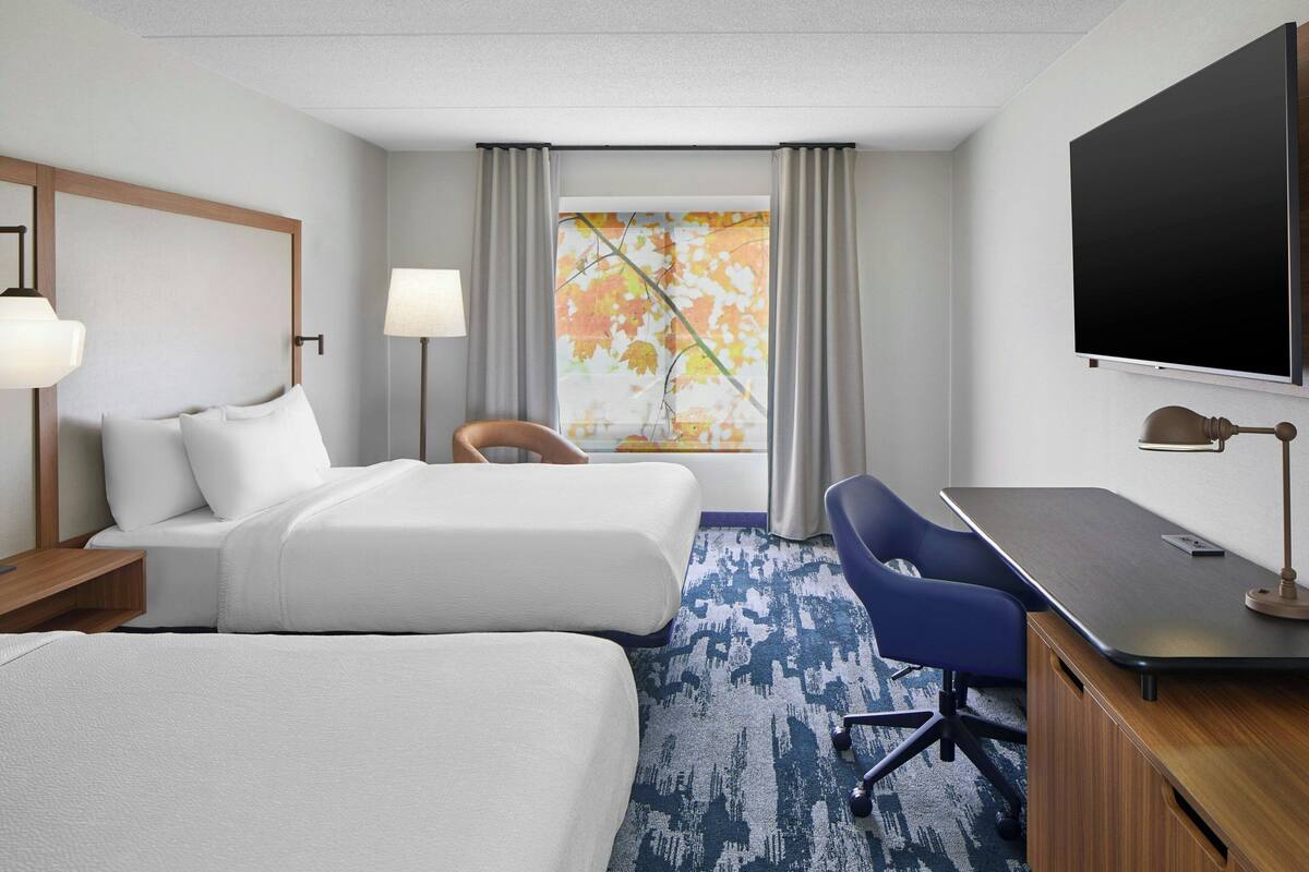 Habitación de hotel con dos camas, un escritorio, una silla, un televisor y una ventana con cortinas.