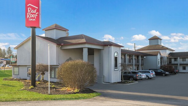 A Red Roof Inn with a two-story structure, a covered parking area, and a small garden with shrubs.