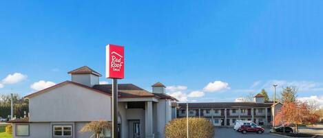 Un hotel Red Roof Inn con cielo azul despejado, un estacionamiento y un edificio con letrero rojo.