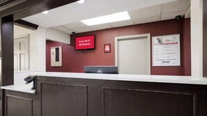 A reception desk with a flat-screen TV displaying 'Free Wi-Fi All Rooms' and a framed RediRewards sign. - Red Roof Inn Weedsport (Weedsport)