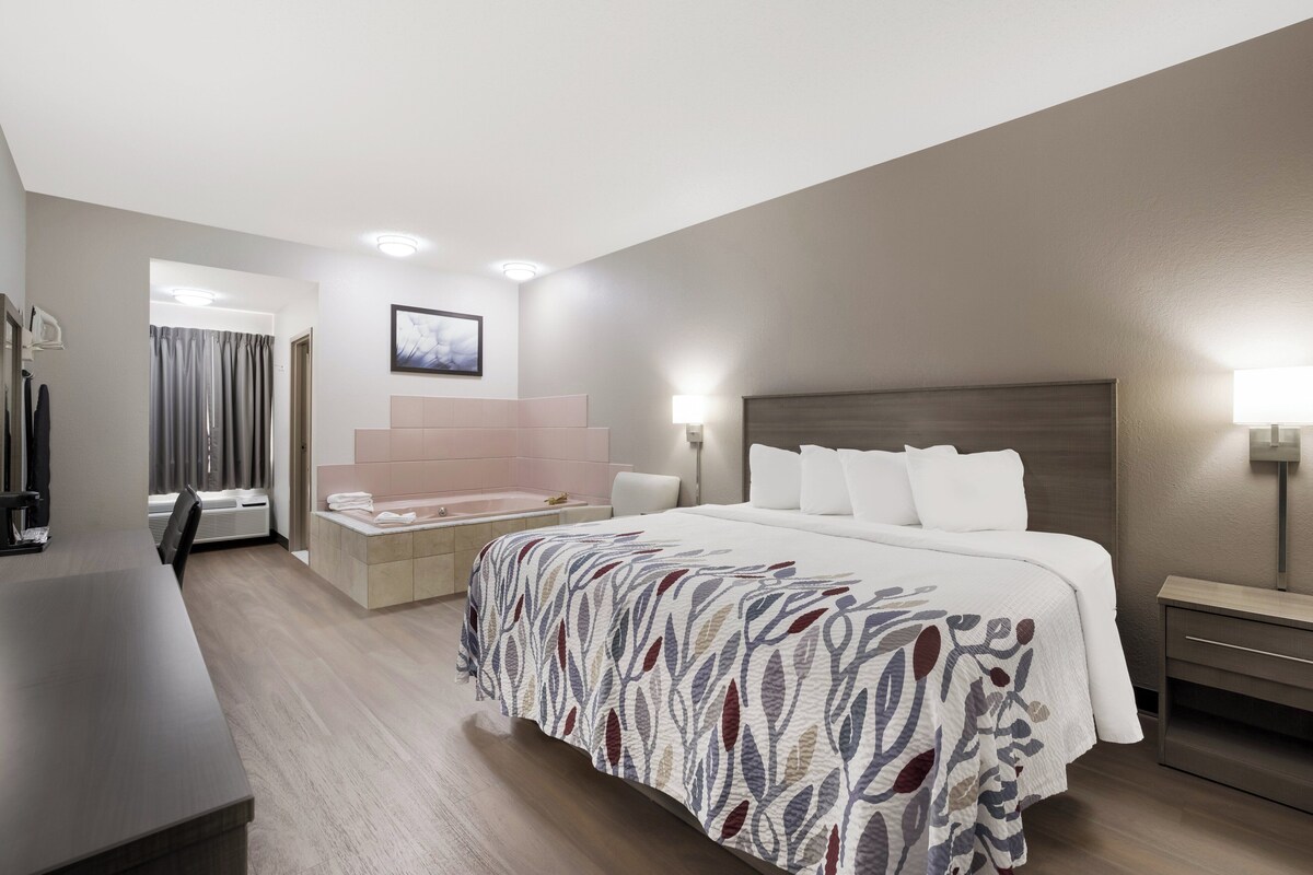 A hotel room with a large bed, a desk, a chair, a vanity with a mirror, and a bathroom with a bathtub.