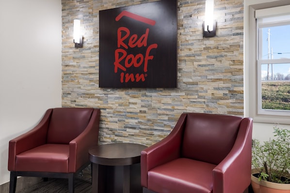 A Red Roof Inn sign on a stone wall, two red leather chairs, and a small round table.