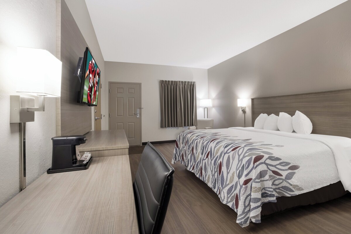 A hotel room with a bed, bedside tables, a TV, a coffee maker, and a door.
