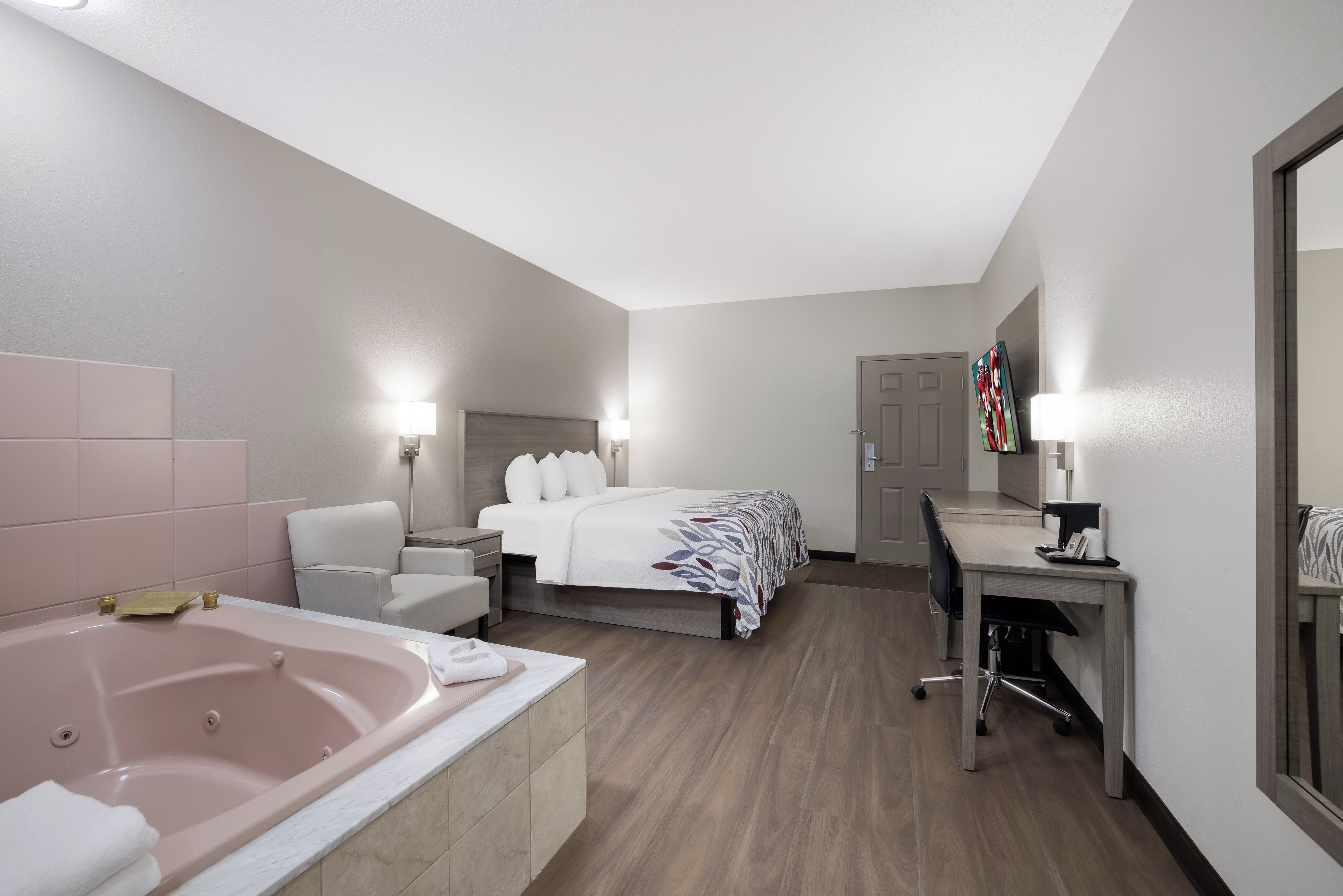 Habitación de hotel con cama, escritorio, silla, lámpara de escritorio, televisor y bañera.