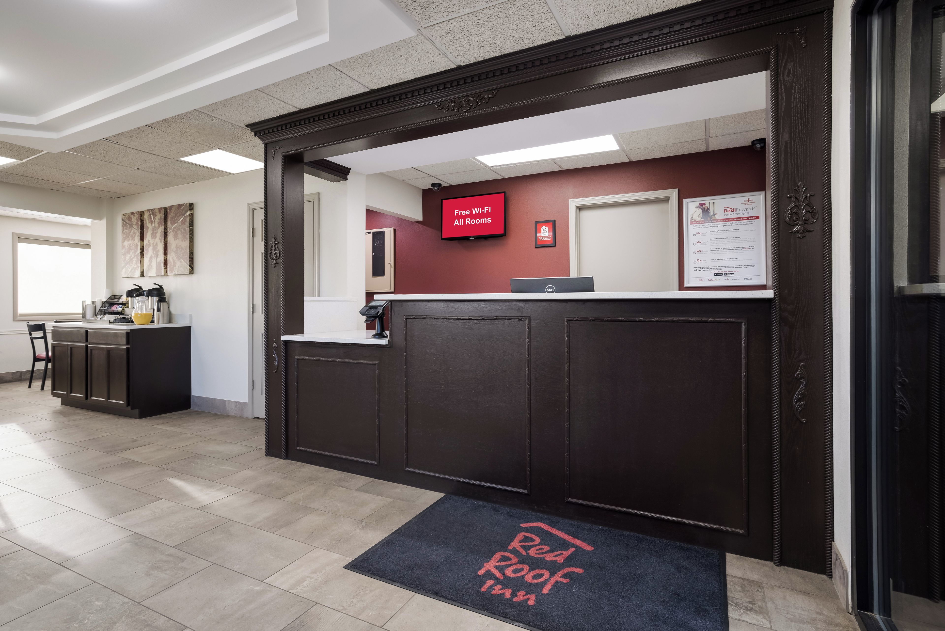 Un espace d’accueil d’hôtel doté d’un écran numérique, d’un comptoir et d’une porte portant l’inscription « Red Roof Inn ».