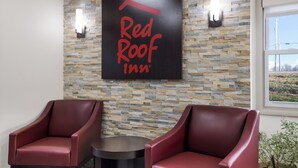 A Red Roof Inn sign on a stone wall, two red leather chairs, and a small round table.