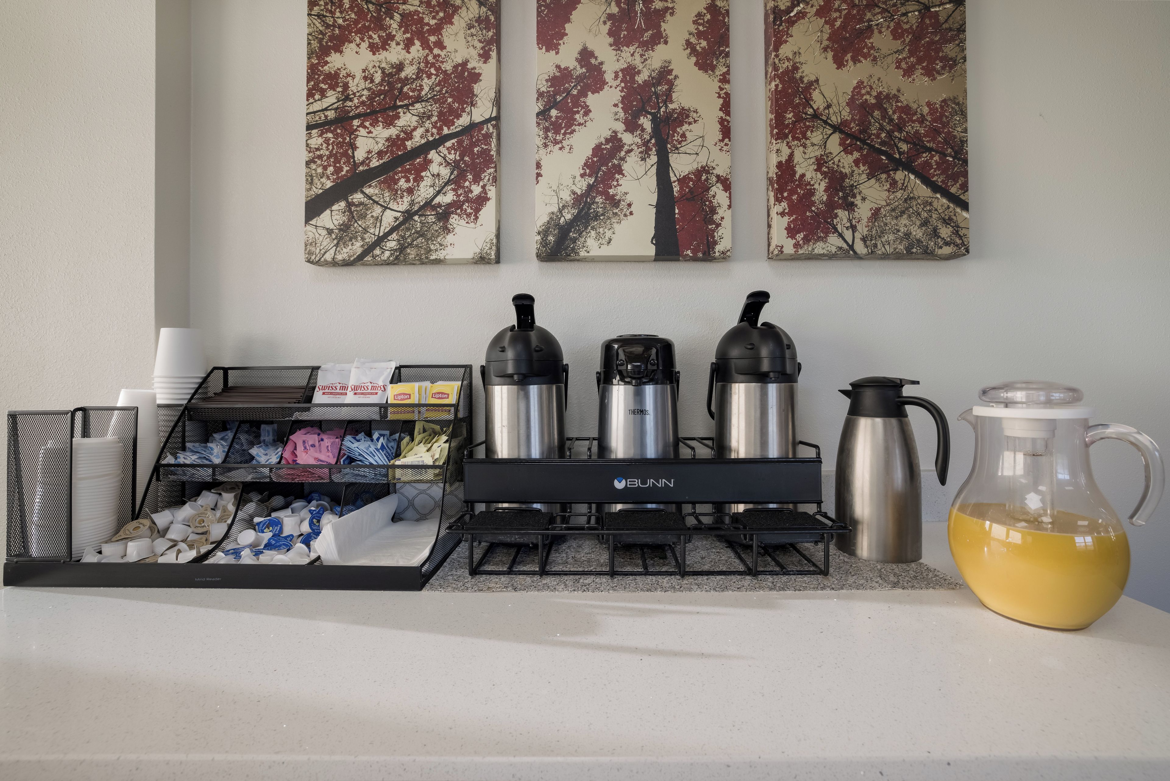 Et tekøkken med kaffemaskine, termokande, elkedel og et kande på bordet.