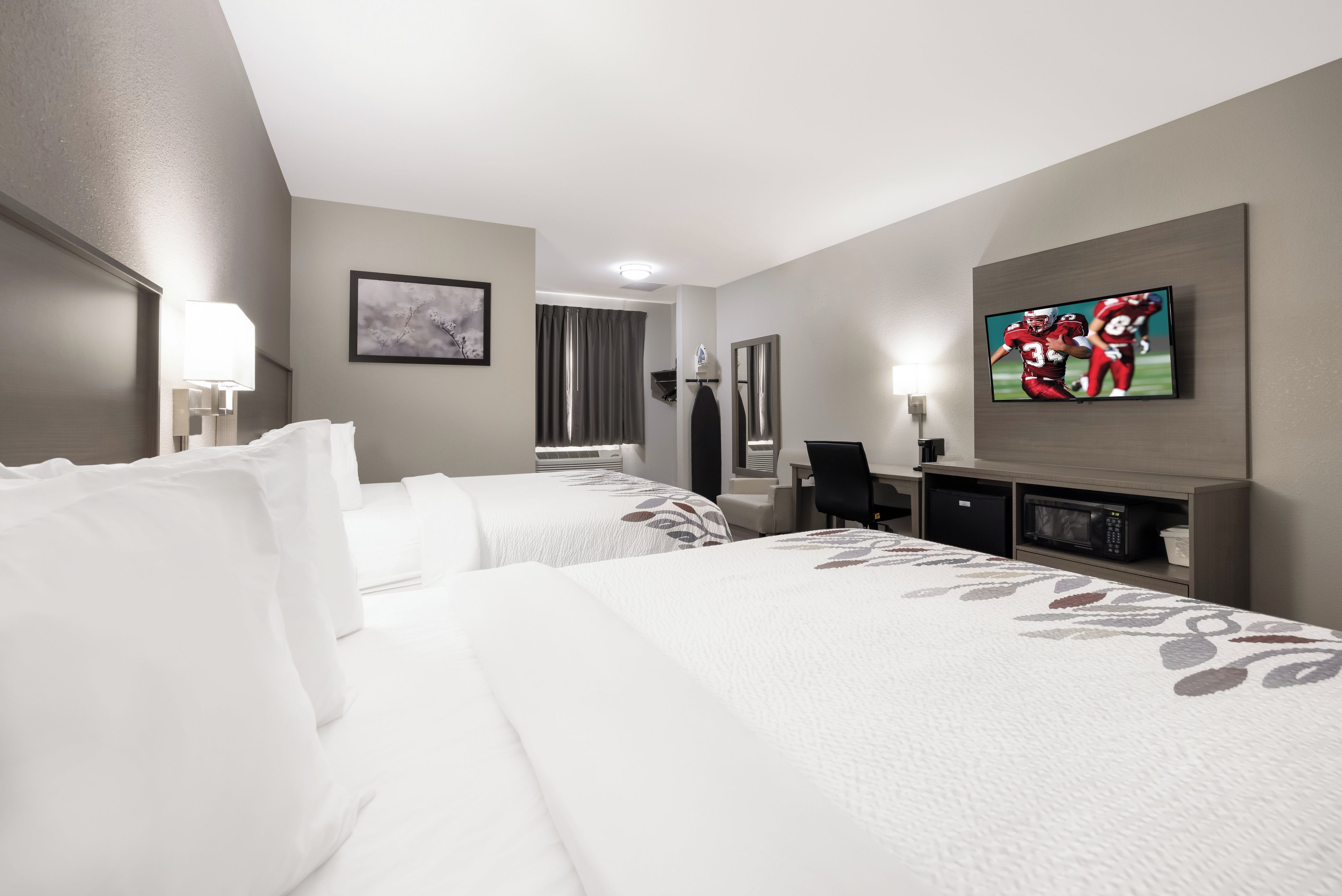 Ein Hotelzimmer mit zwei Betten, einem Flachbildfernseher, einem Schreibtisch und einem Spiegel.