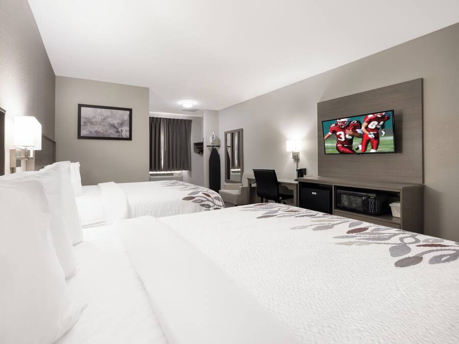 A hotel room with two beds, a flat-screen TV, a desk, and a mirror.