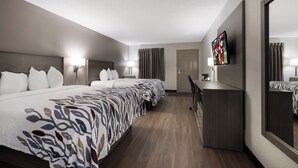 A hotel room with a large bed, a desk, a TV, and a door.