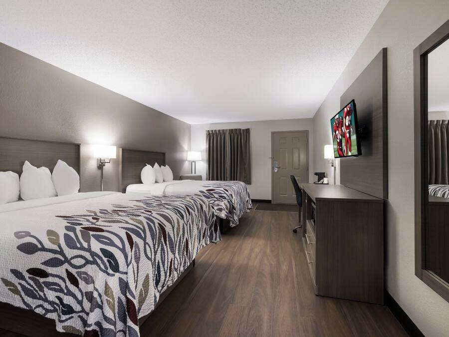 A hotel room with a large bed, a desk, a TV, and a door.