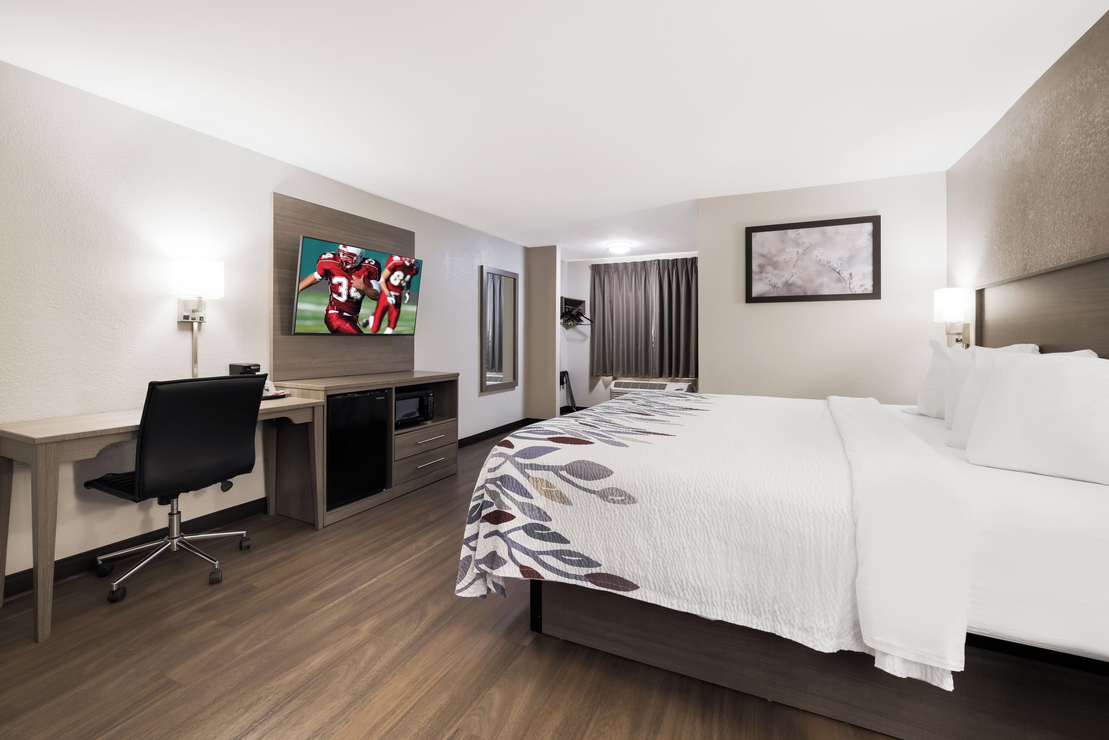 A hotel room with a bed, desk, chair, television, and a bathroom with a shower curtain.