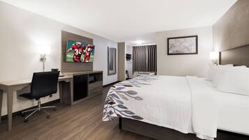 Quarto de hotel com cama, escrivaninha, cadeira, televisão e banheiro com cortina de chuveiro.
