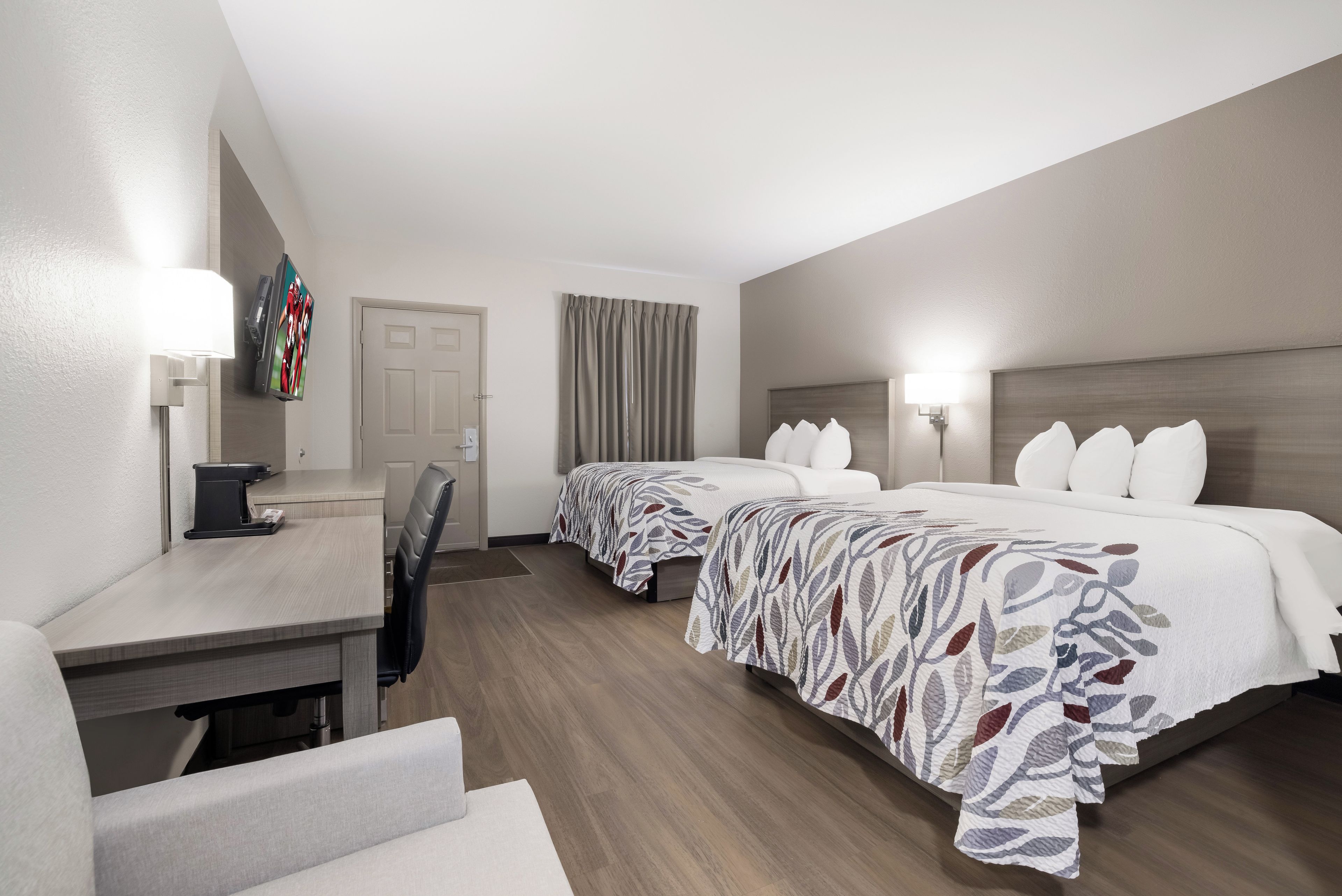 Une chambre d’hôtel avec deux lits, un bureau, une chaise et un téléviseur.