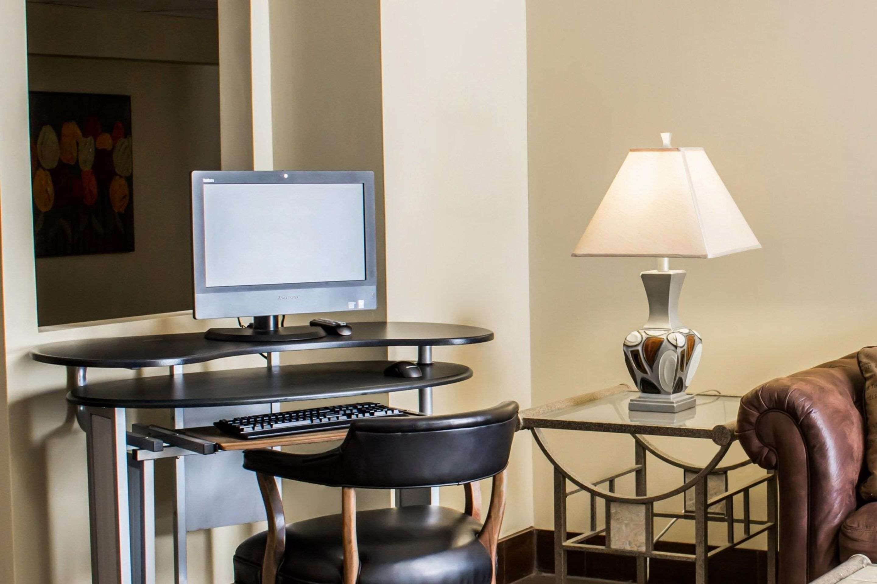 Una habitación moderna con escritorio, computadora, teclado, silla, lámpara y un sofá de cuero.