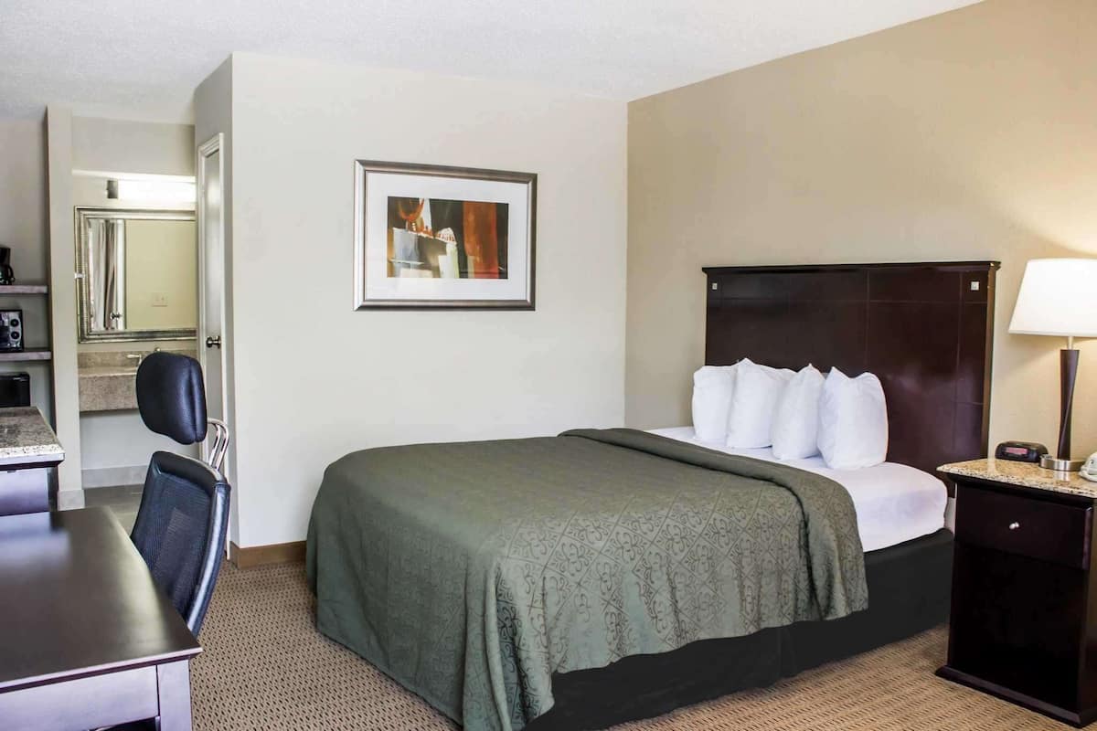 A hotel room with a bed, a desk, a chair, a lamp, and a framed picture on the wall.