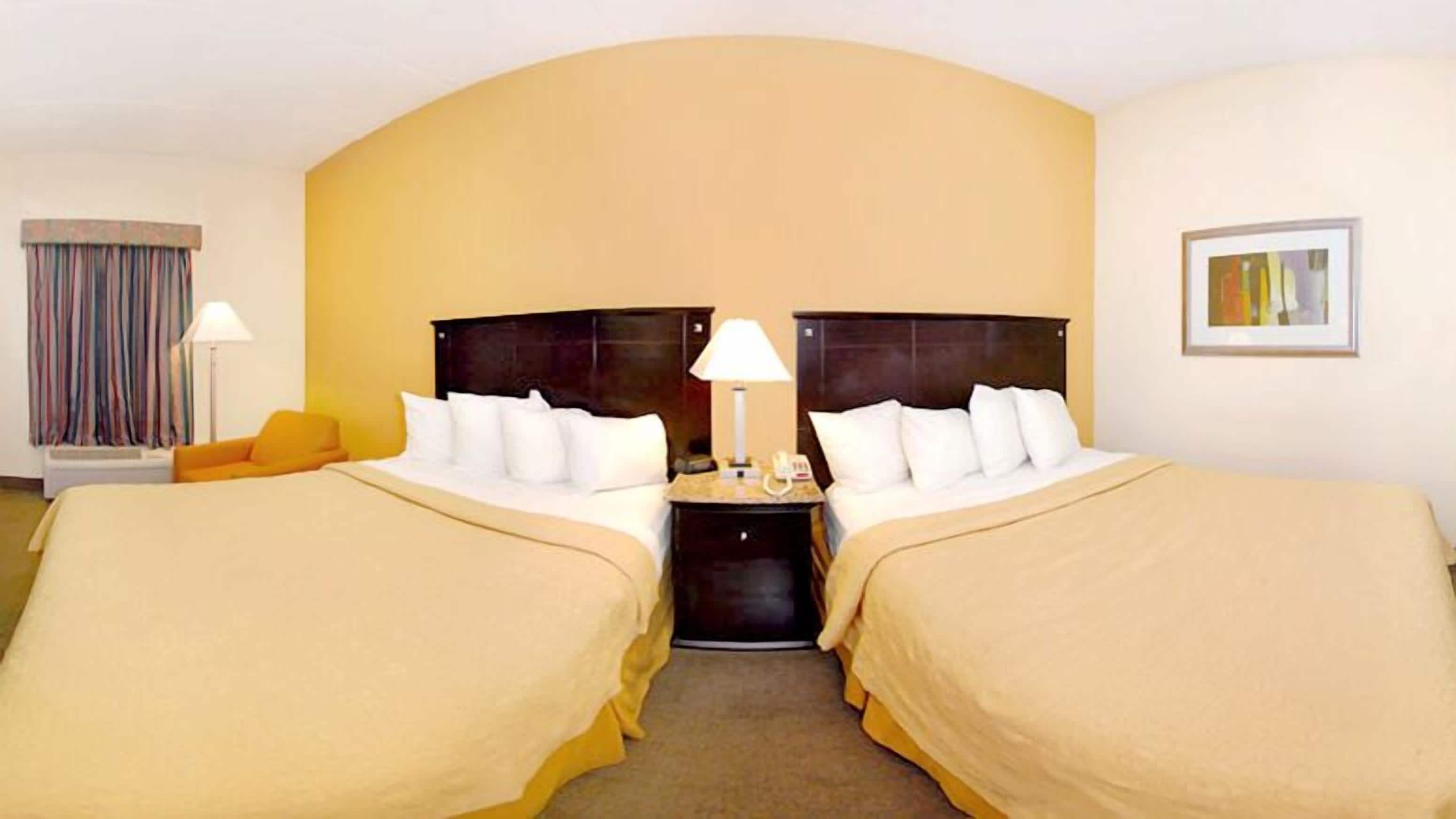 A hotel room with two beds, a nightstand, a lamp, a telephone, and a painting on the wall.
