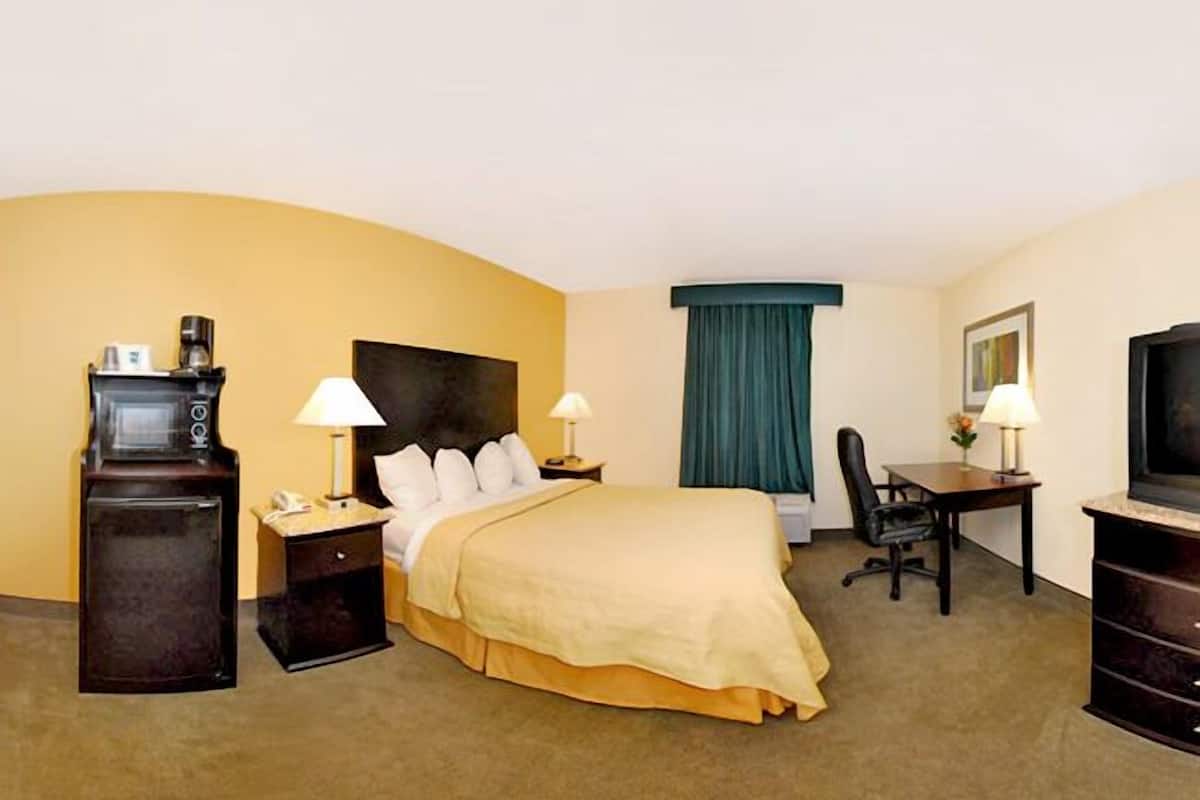 A hotel room with a bed, bedside tables, a desk, a chair, a television, and a coffee machine.