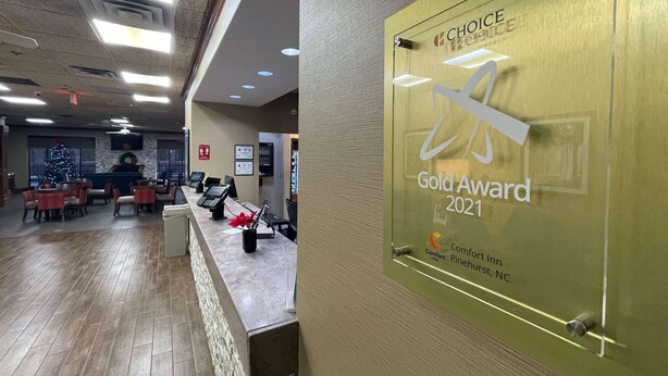 Uma área de recepção de hotel com uma placa de 'Prêmio de Ouro 2021', um balcão de recepção e uma sala de jantar com mesas e cadeiras.