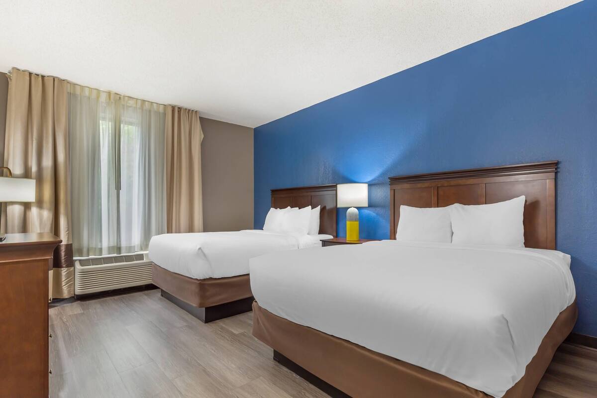 A hotel room with two beds, a desk, a lamp, and a window with curtains.