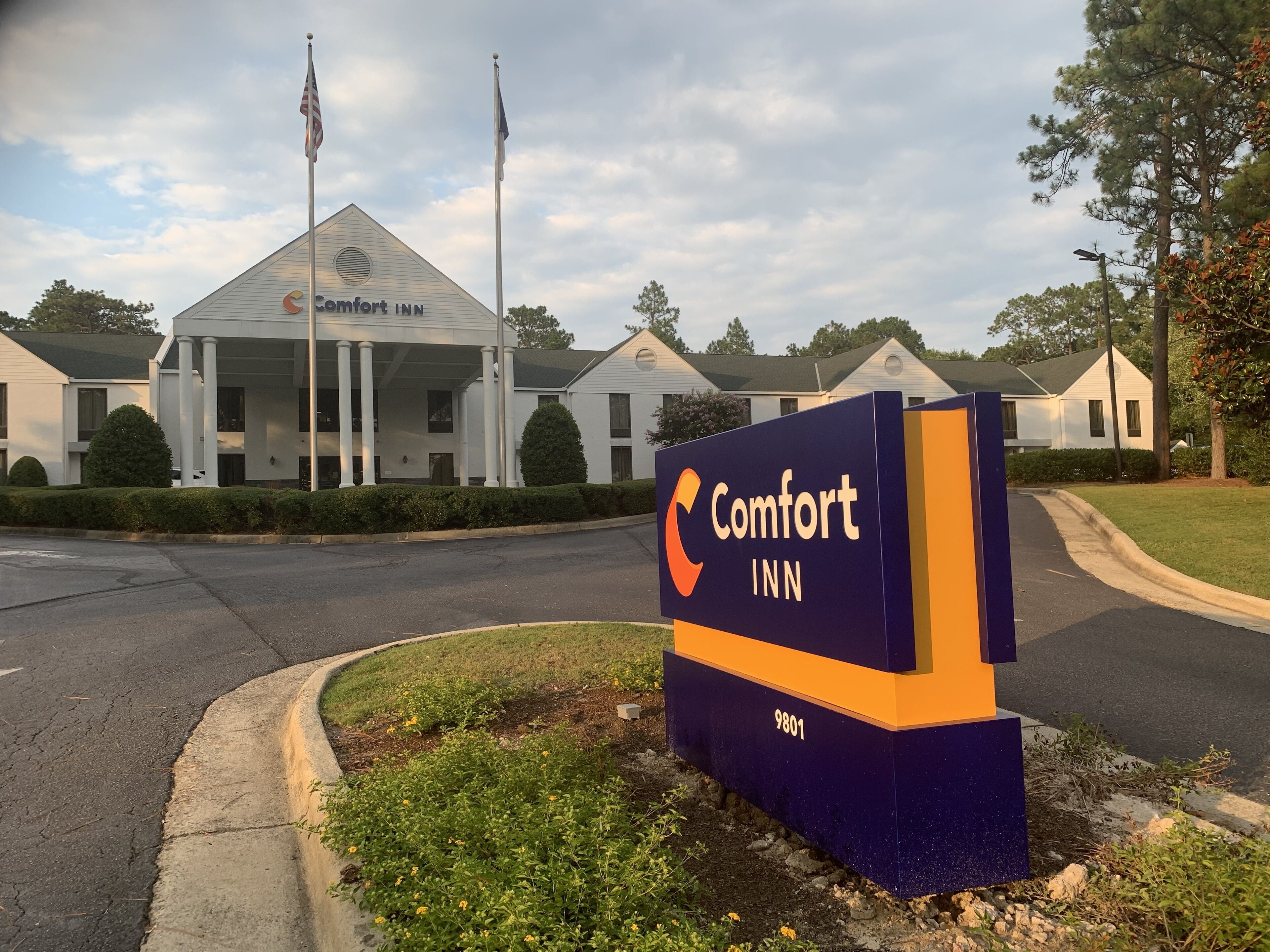 A Comfort Inn sign with a modern design, located in a suburban area with a well-maintained lawn and a road in front.