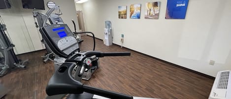 Un gimnasio con cintas de correr, equipo de ejercicio y decoración inspiradora en las paredes.