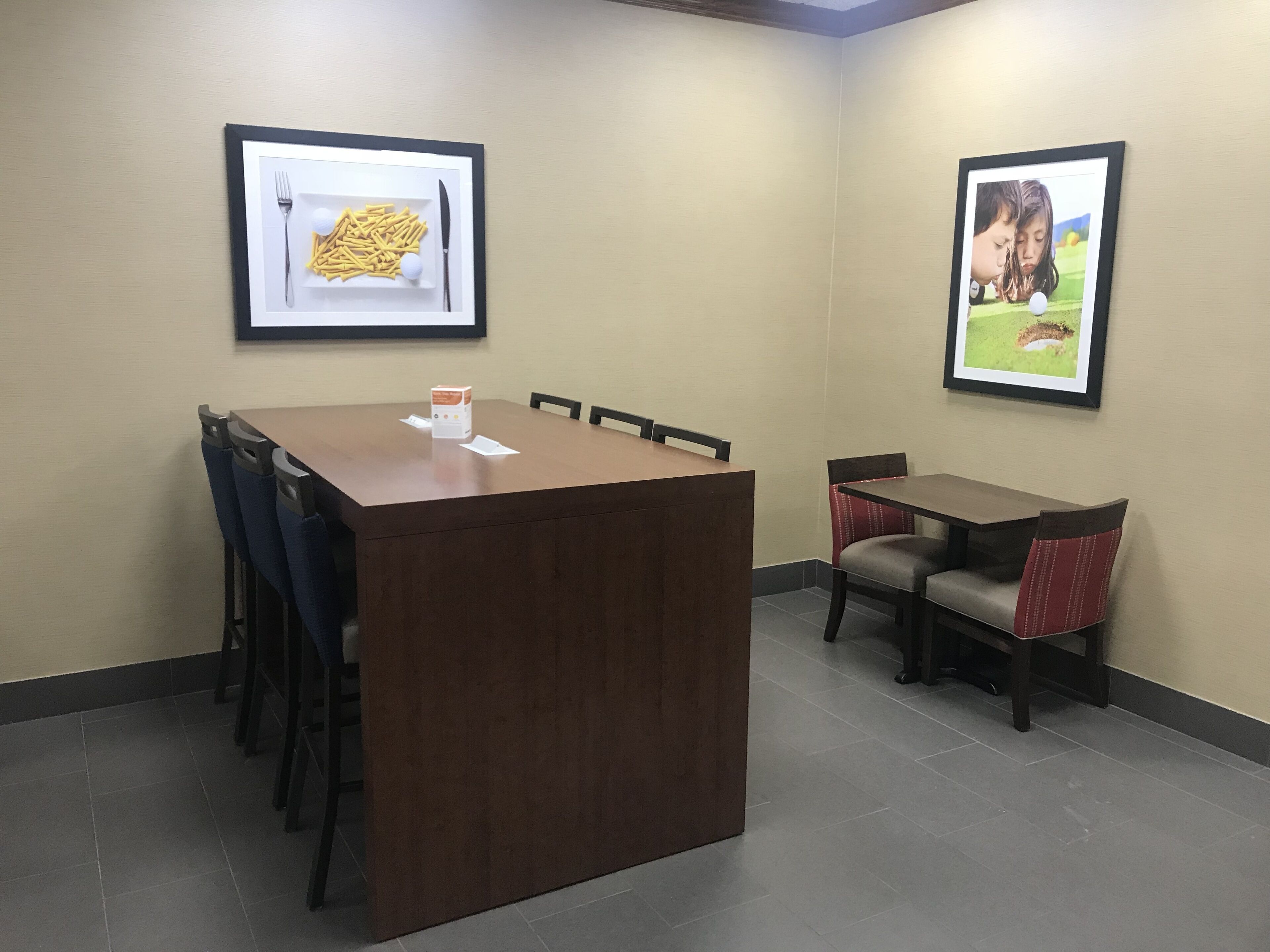 A conference room with a wooden table and chairs, framed pictures on the walls, and a tiled floor.