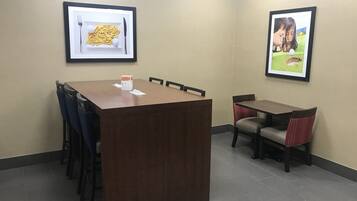 A conference room with a wooden table and chairs, framed pictures on the walls, and a tiled floor.
