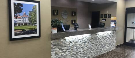 Un mostrador de recepción con una pared de piedra, un cuadro de un edificio y un cartel que dice "Comfort Inn".