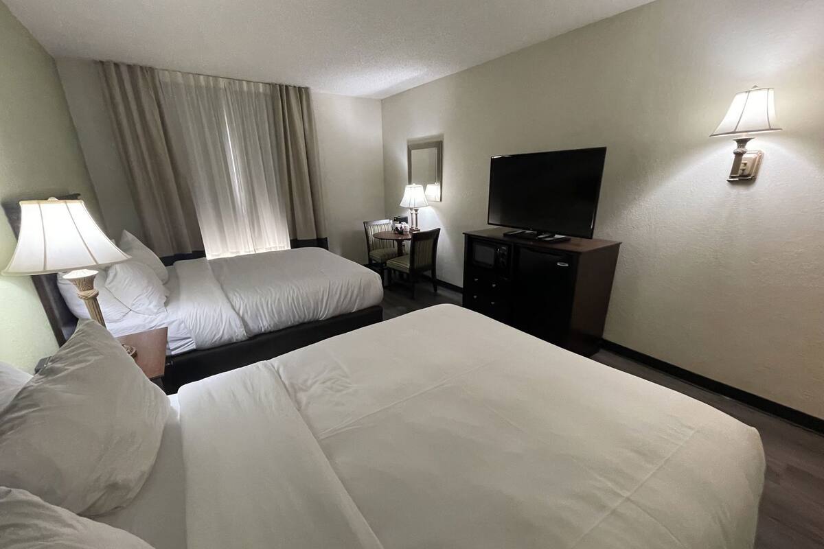 A hotel room with two beds, a TV, a desk with a lamp, and a dresser.