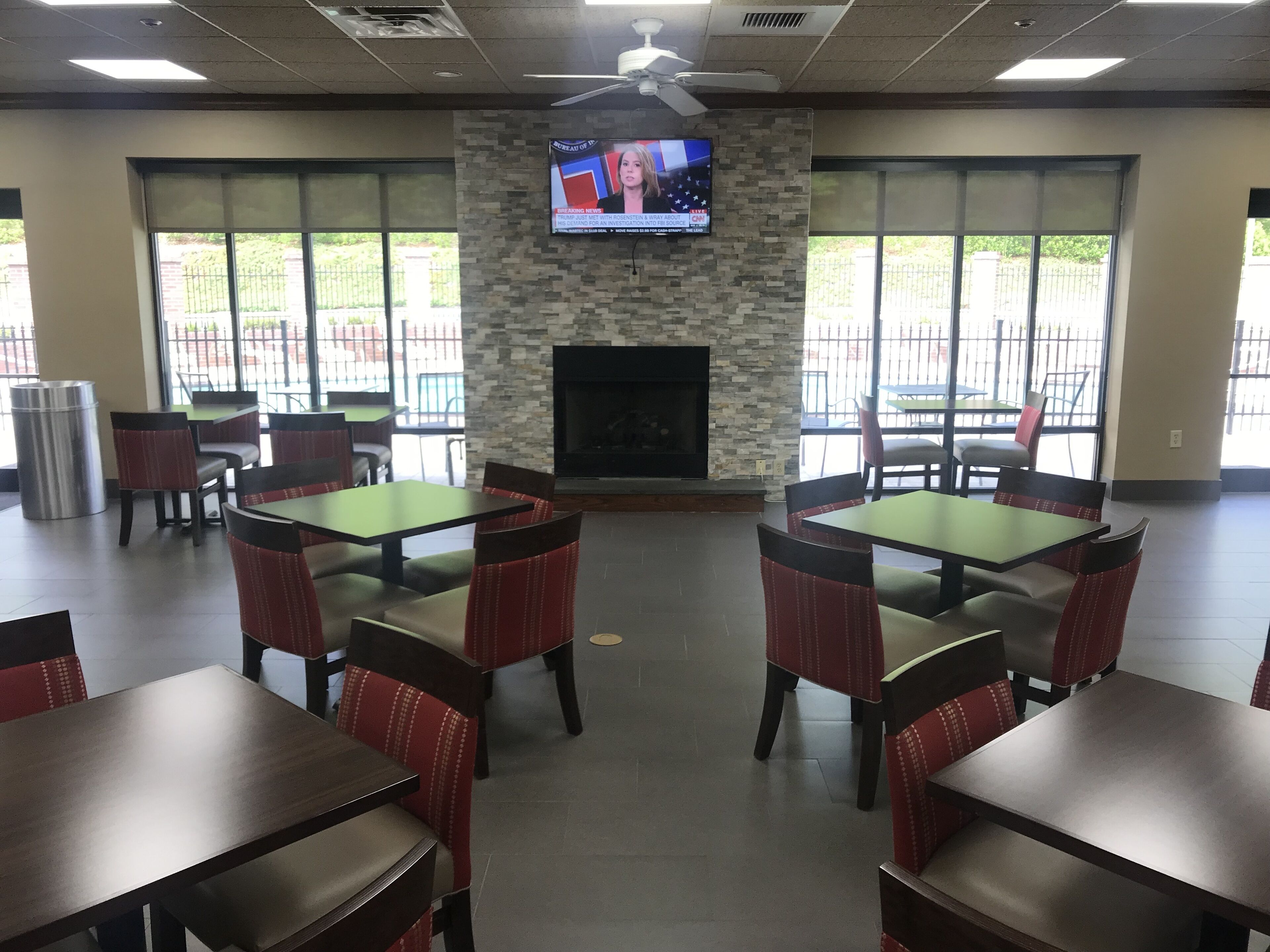 A restaurant with multiple tables and chairs, a television mounted on a stone wall, and a fireplace.