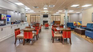 Um saguão de hotel com várias mesas e cadeiras para refeições, uma lareira, uma televisão fixada em uma parede de pedra e um espaço de estar com sofás e poltronas.