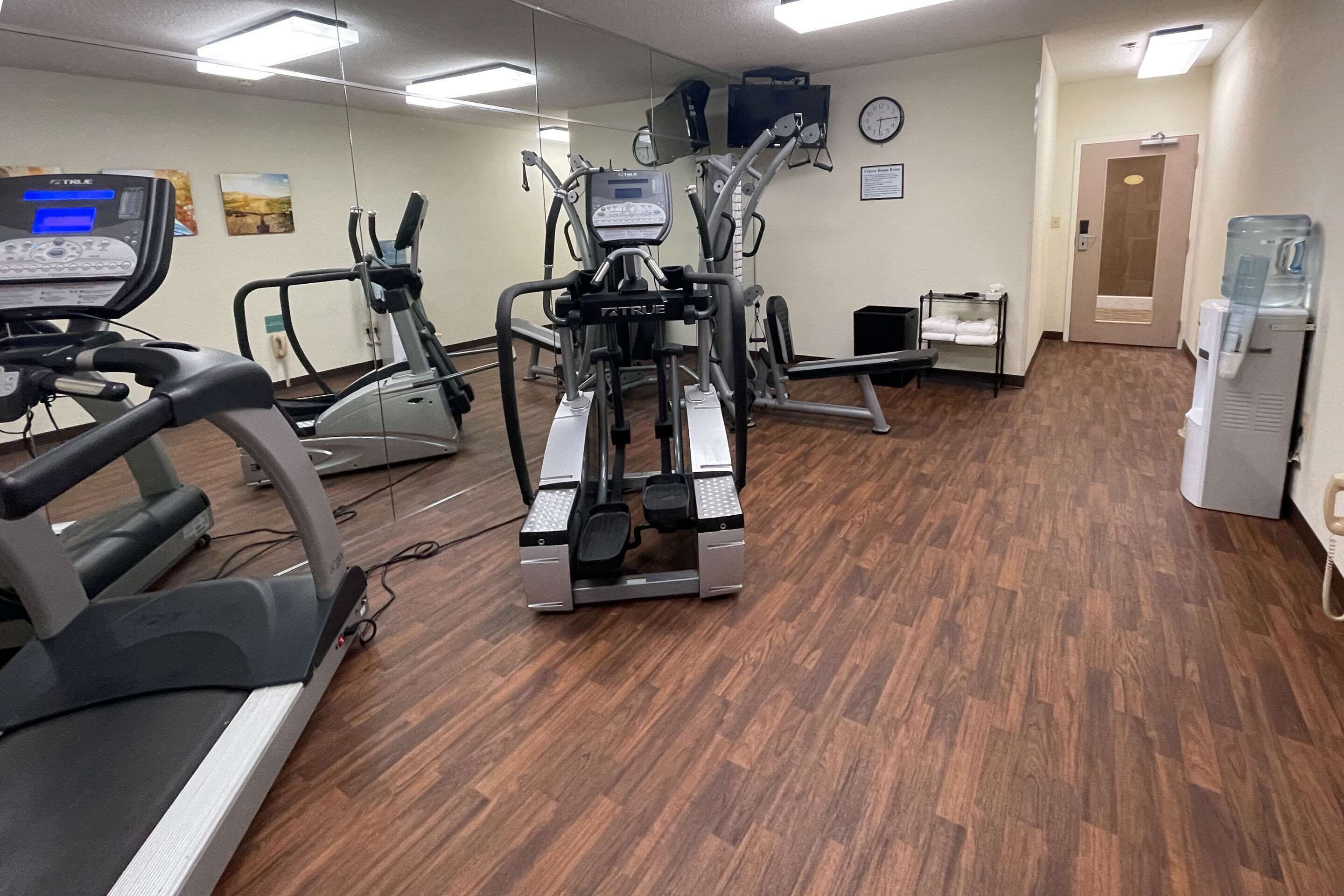 Un gimnasio con diferentes máquinas de ejercicio, un dispensador de agua y un reloj en la pared.