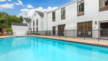 Piscina adjacente a um edifício branco com janelas amplas e um espaço de pátio cercado.
