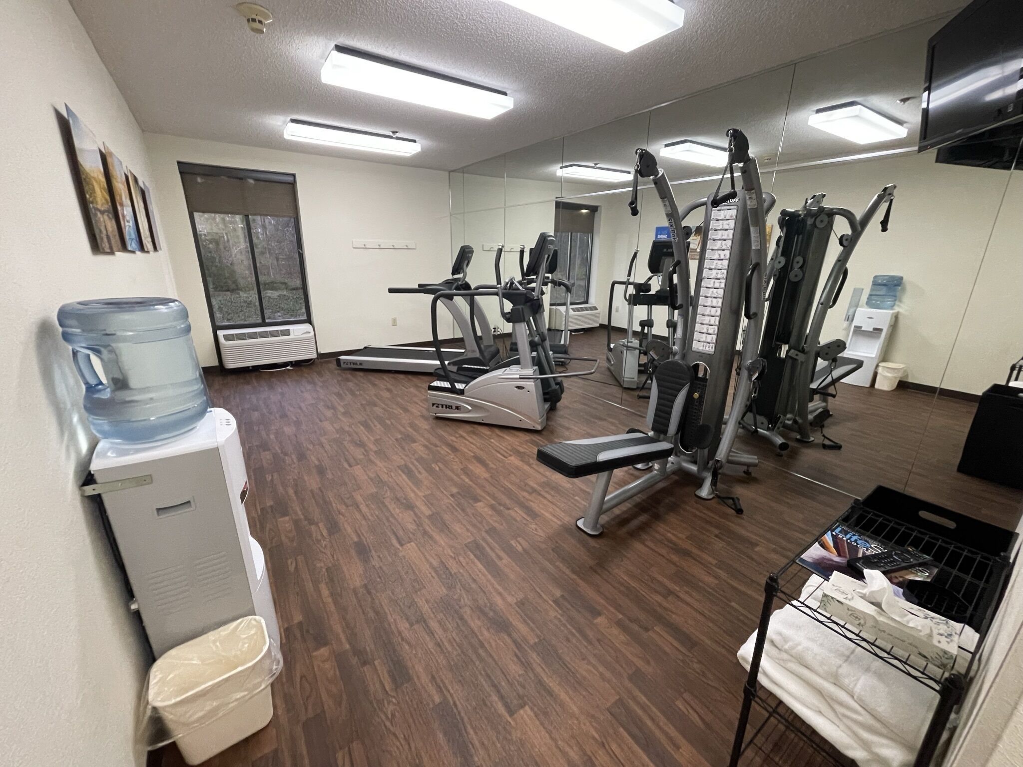 Un gimnasio con diversos equipos de ejercicio, un dispensador de agua y un enfriador grande.