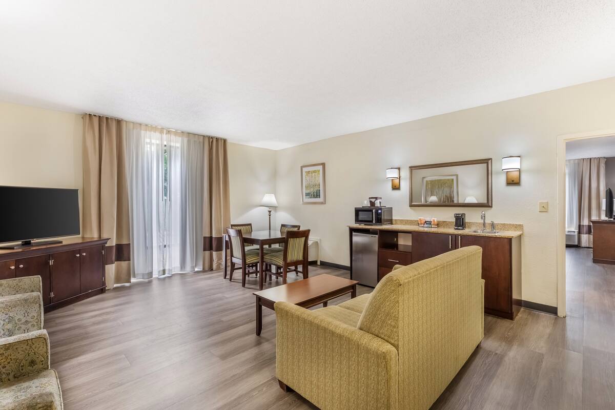 A hotel room with a living area, a dining table, a kitchen, and a TV.