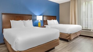 A hotel room with two beds, a nightstand, a lamp, and a window with curtains.