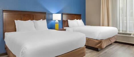A hotel room with two beds, a nightstand, a lamp, and a window with curtains.