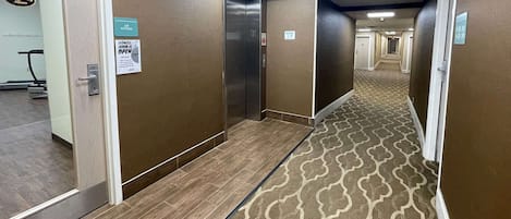 Un pasillo de hotel con alfombra estampada, un letrero que indica gimnasio y un ascensor.