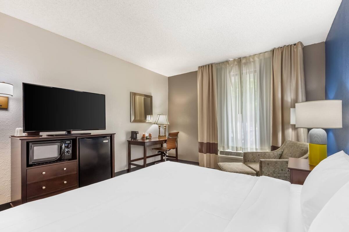 A hotel room with a bed, a desk with a computer, a television, a microwave, and a refrigerator.