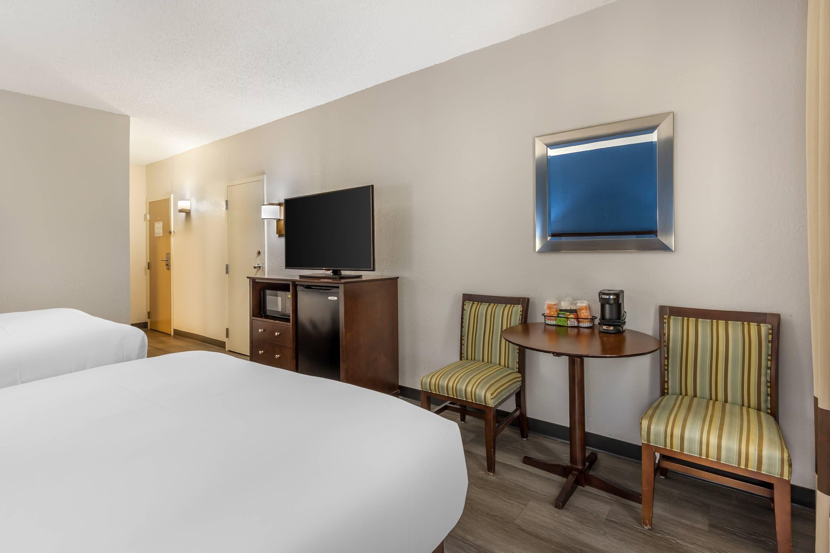 A hotel room with two beds, a TV, a small table with a coffee maker, and two striped chairs.