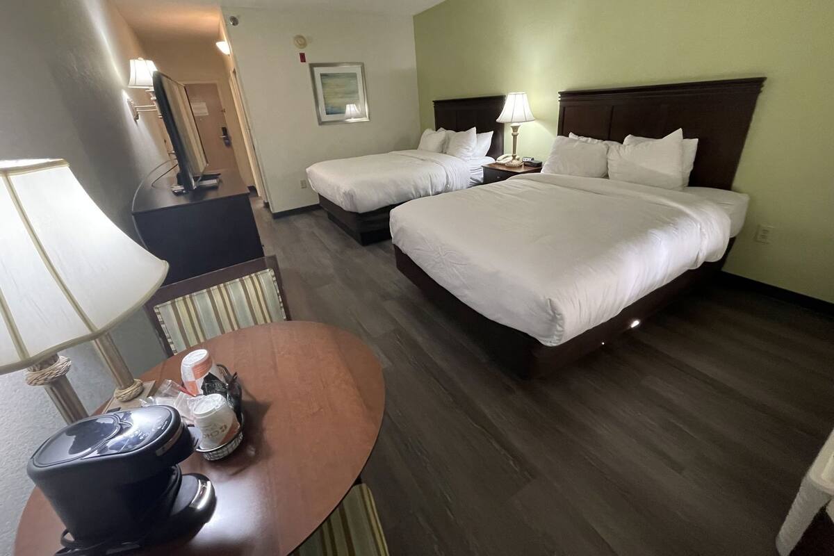 A hotel room with two beds, a desk with a lamp, a chair, and a small table with a coffee maker.